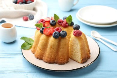 Photo of Tasty Bundt cake with berries, honey and mint on light blue wooden table, closeup