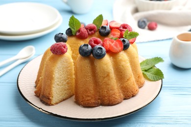 Photo of Tasty Bundt cake with berries, honey and mint on light blue wooden table, closeup