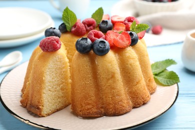 Photo of Tasty Bundt cake with berries and mint on light blue wooden table, closeup