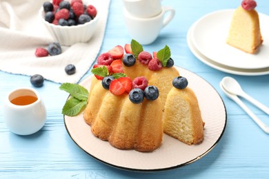 Photo of Tasty Bundt cake with berries, honey and mint on light blue wooden table, closeup