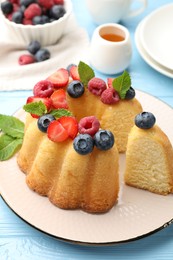 Photo of Tasty Bundt cake with berries, honey and mint on light blue wooden table, closeup
