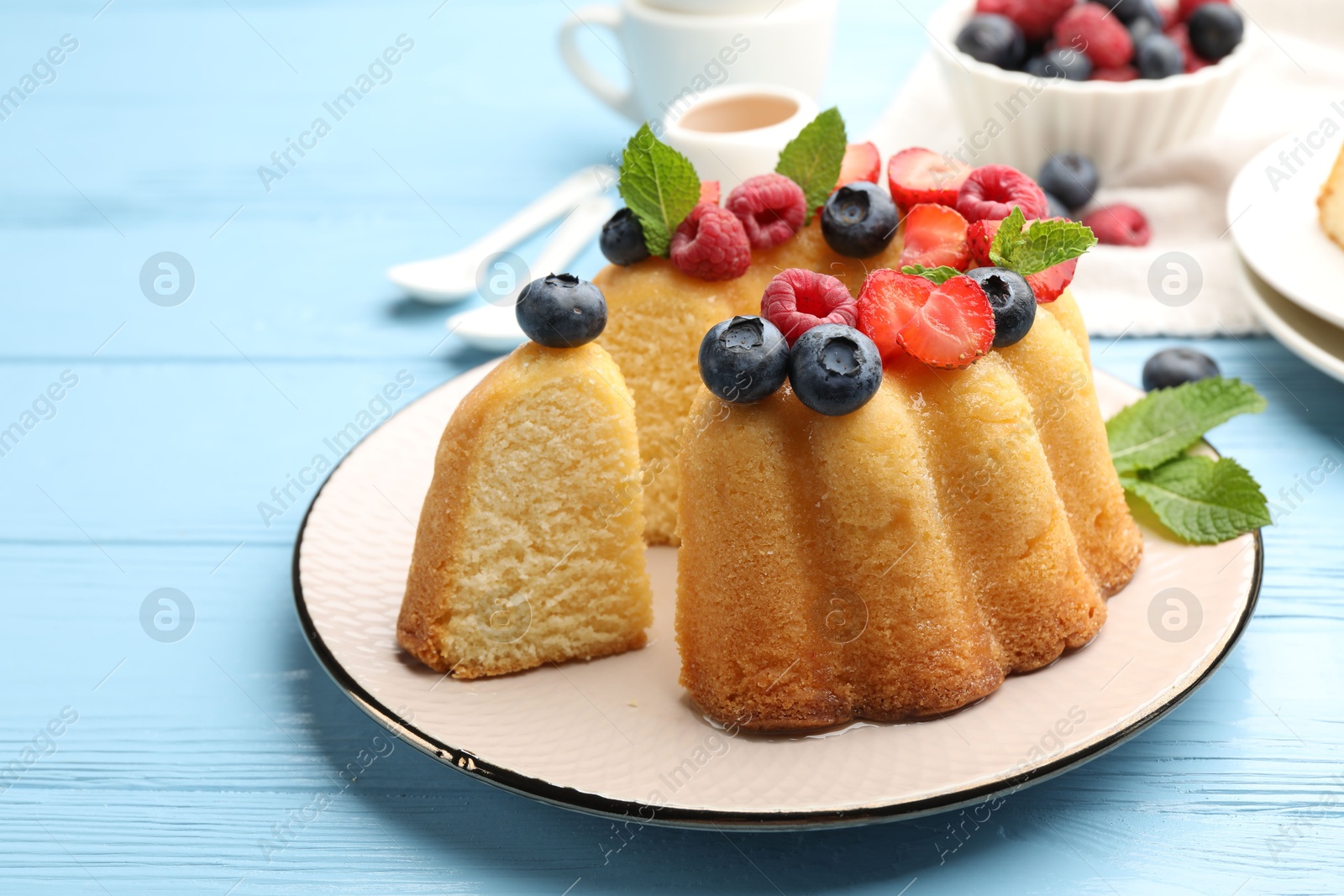 Photo of Tasty Bundt cake with berries and mint on light blue wooden table, closeup