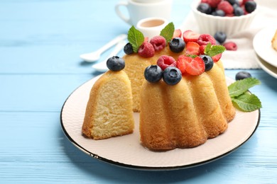Photo of Tasty Bundt cake with berries and mint on light blue wooden table, closeup