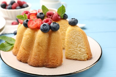 Photo of Tasty Bundt cake with berries and mint on light blue wooden table, closeup