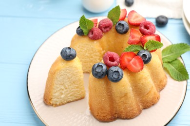 Photo of Tasty Bundt cake with berries and mint on light blue wooden table, closeup