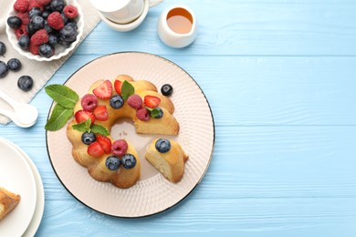 Photo of Tasty Bundt cake with berries, honey and mint on light blue wooden table, flat lay. Space for text