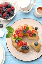 Photo of Tasty Bundt cake with berries, honey and mint on light blue wooden table, flat lay