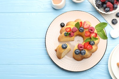 Photo of Tasty Bundt cake with berries, honey and mint on light blue wooden table, flat lay. Space for text