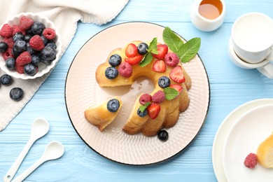 Photo of Tasty Bundt cake with berries, honey and mint on light blue wooden table, flat lay