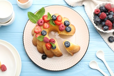 Photo of Tasty Bundt cake with berries, honey and mint on light blue wooden table, flat lay