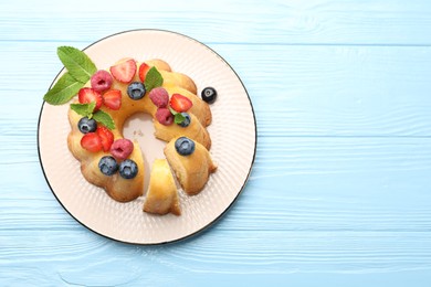 Photo of Tasty Bundt cake with berries and mint on light blue wooden table, top view. Space for text