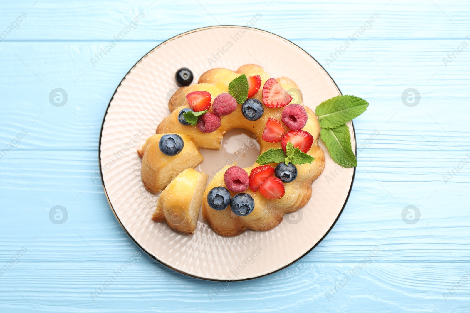 Tasty Bundt cake with berries and mint on light blue wooden table, top view Photo of Tasty Bundt cake with berries and mint on light blue wooden table, top view