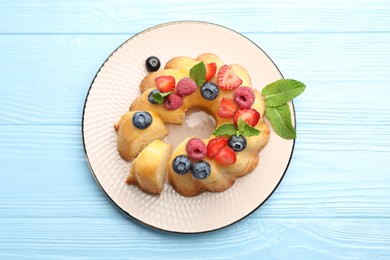 Photo of Tasty Bundt cake with berries and mint on light blue wooden table, top view