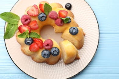 Photo of Tasty Bundt cake with berries and mint on light blue wooden table, top view