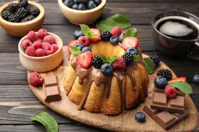 Photo of Tasty Bundt cake with berries, chocolate, mint and coffee on wooden table, closeup