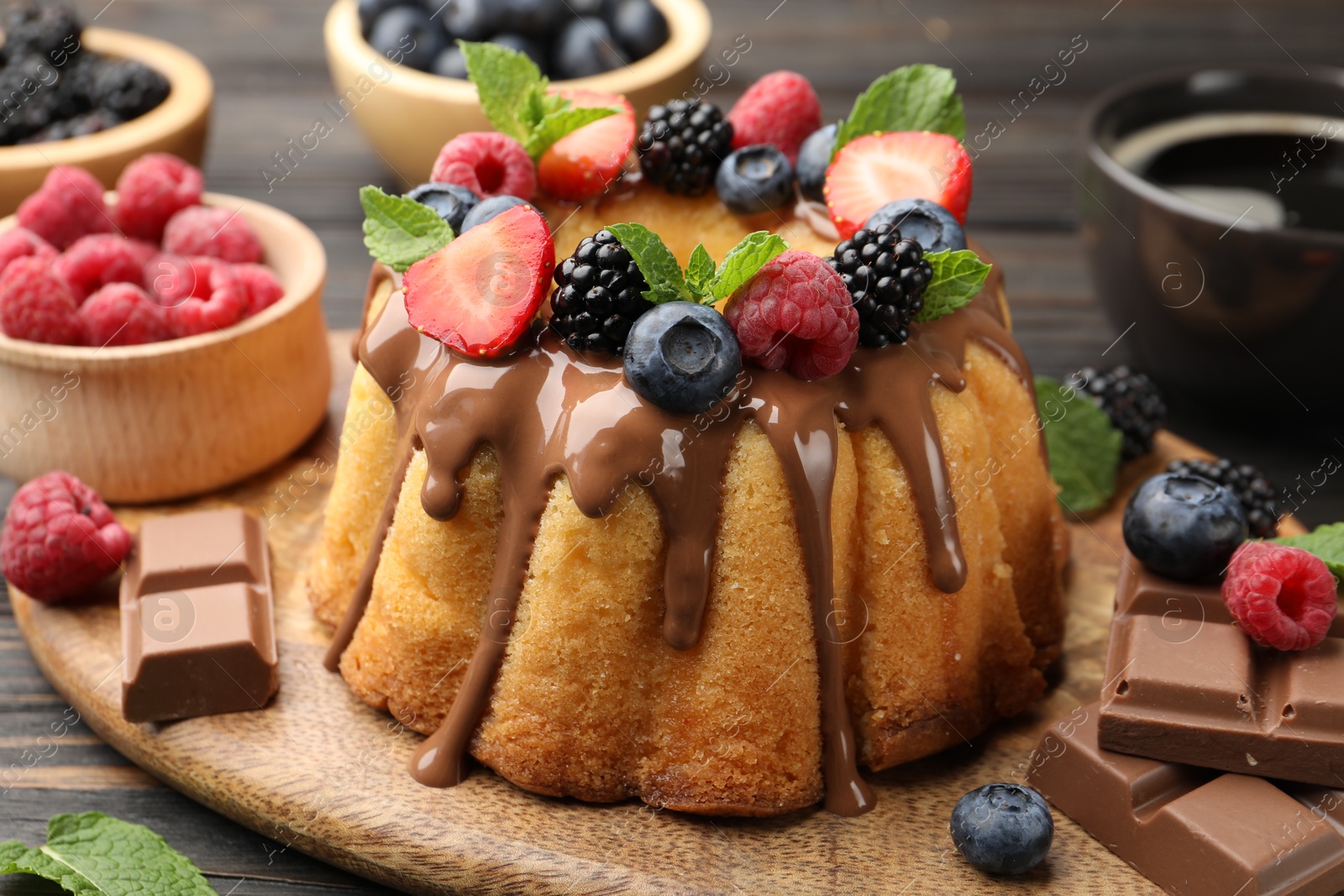 Photo of Tasty Bundt cake with berries, chocolate, mint and coffee on wooden table, closeup