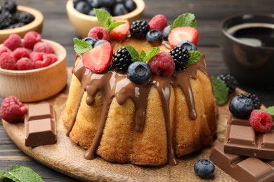 Photo of Tasty Bundt cake with berries, chocolate, mint and coffee on wooden table, closeup