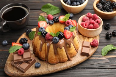 Photo of Tasty Bundt cake with berries, chocolate, mint and coffee on wooden table, closeup