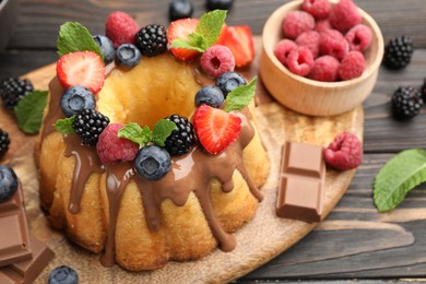 Photo of Tasty Bundt cake with berries, chocolate and mint on wooden table, closeup