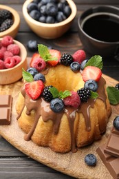 Photo of Tasty Bundt cake with berries, chocolate, mint and coffee on wooden table, closeup