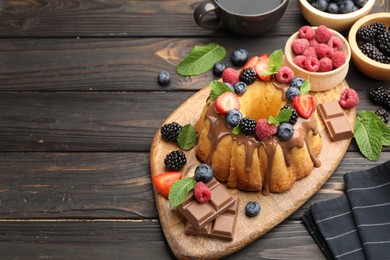 Photo of Tasty Bundt cake with berries, chocolate, mint and coffee on wooden table, above view. Space for text