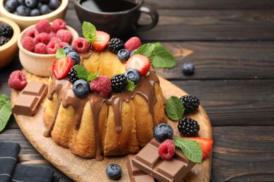 Photo of Tasty Bundt cake with berries, chocolate, mint and coffee on wooden table, closeup. Space for text
