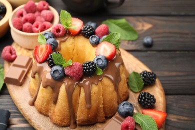 Photo of Tasty Bundt cake with berries, chocolate and mint on wooden table, closeup