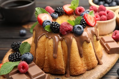 Photo of Tasty Bundt cake with berries, chocolate, mint and coffee on wooden table, closeup