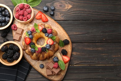Photo of Tasty Bundt cake with berries, chocolate and mint on wooden table, flat lay. Space for text