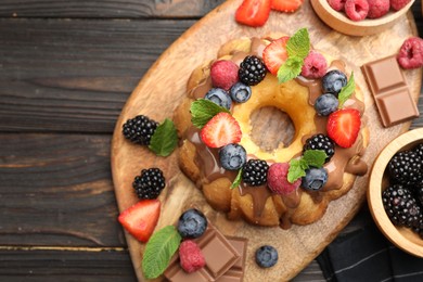 Photo of Tasty Bundt cake with berries, chocolate and mint on wooden table, top view. Space for text