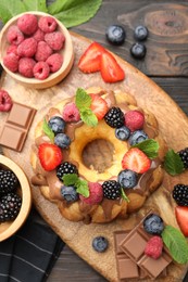 Photo of Tasty Bundt cake with berries, chocolate and mint on wooden table, top view