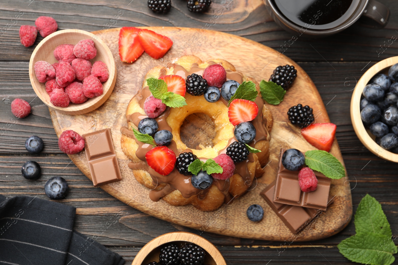 Tasty Bundt cake with berries, chocolate, mint and coffee on wooden table, flat lay Photo of Tasty Bundt cake with berries, chocolate, mint and coffee on wooden table, flat lay