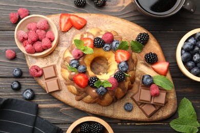 Photo of Tasty Bundt cake with berries, chocolate, mint and coffee on wooden table, flat lay