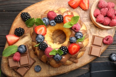 Photo of Tasty Bundt cake with berries, chocolate and mint on wooden table, top view