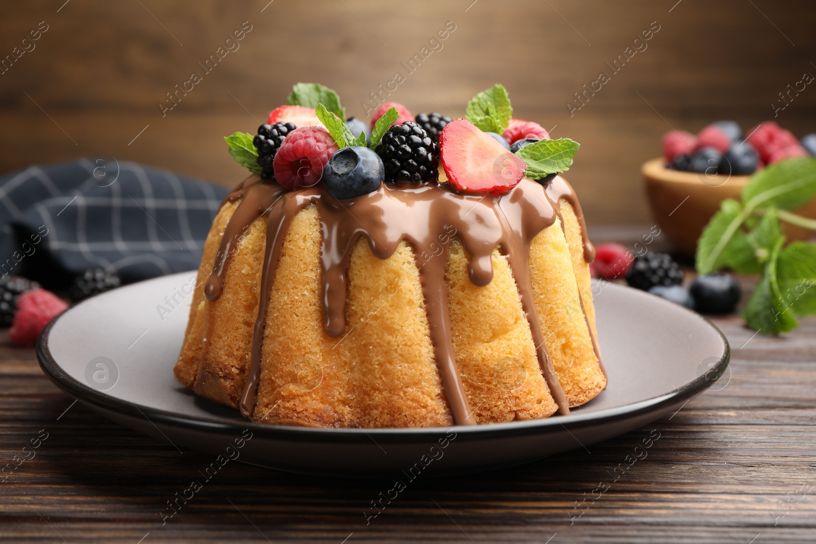 Tasty Bundt cake with berries, chocolate and mint on wooden table, closeup Photo of Tasty Bundt cake with berries, chocolate and mint on wooden table, closeup