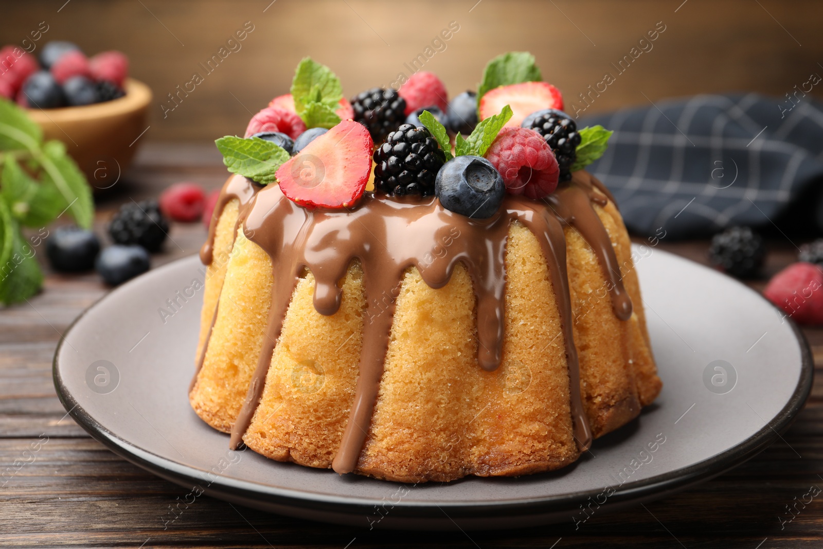 Tasty Bundt cake with berries, chocolate and mint on wooden table, closeup Photo of Tasty Bundt cake with berries, chocolate and mint on wooden table, closeup
