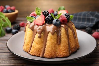 Photo of Tasty Bundt cake with berries, chocolate and mint on wooden table, closeup