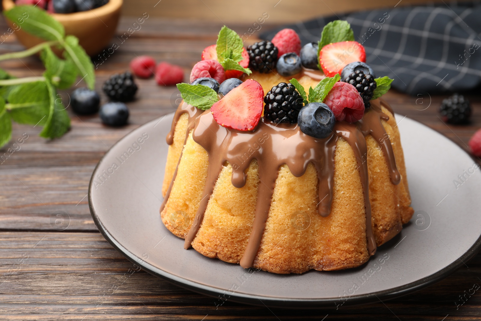 Tasty Bundt cake with berries, chocolate and mint on wooden table, closeup Photo of Tasty Bundt cake with berries, chocolate and mint on wooden table, closeup