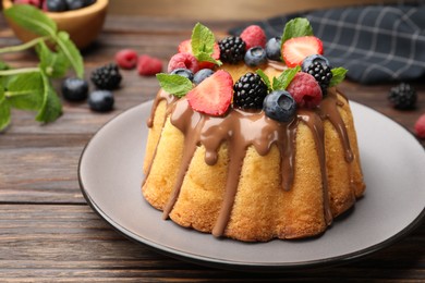 Photo of Tasty Bundt cake with berries, chocolate and mint on wooden table, closeup