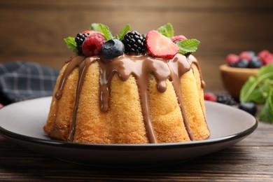 Photo of Tasty Bundt cake with berries, chocolate and mint on wooden table, closeup