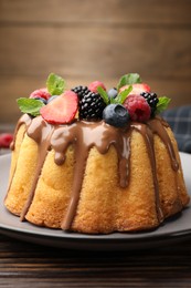 Photo of Tasty Bundt cake with berries, chocolate and mint on wooden table, closeup