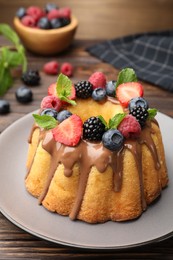 Photo of Tasty Bundt cake with berries, chocolate and mint on wooden table, closeup
