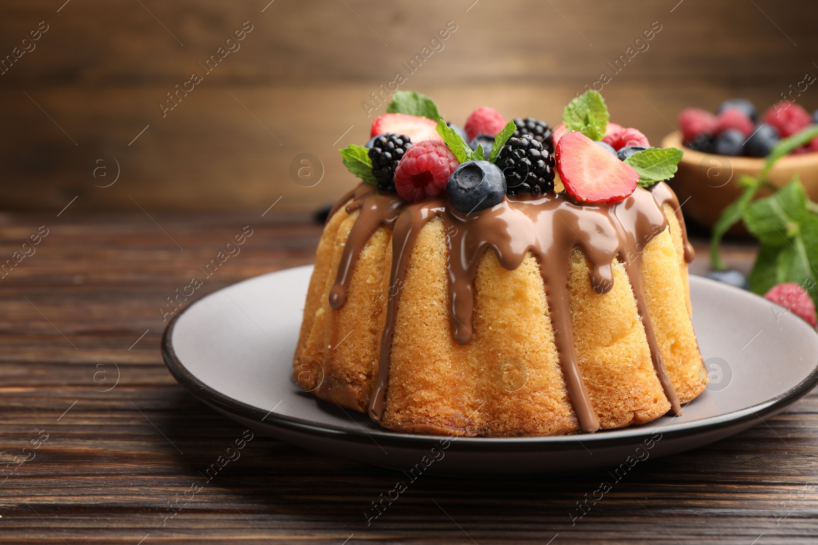 Tasty Bundt cake with berries, chocolate and mint on wooden table, closeup Photo of Tasty Bundt cake with berries, chocolate and mint on wooden table, closeup