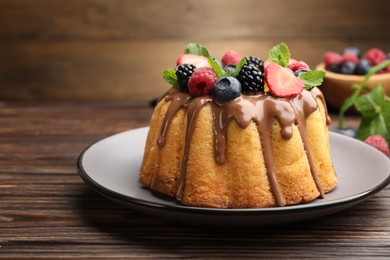 Photo of Tasty Bundt cake with berries, chocolate and mint on wooden table, closeup