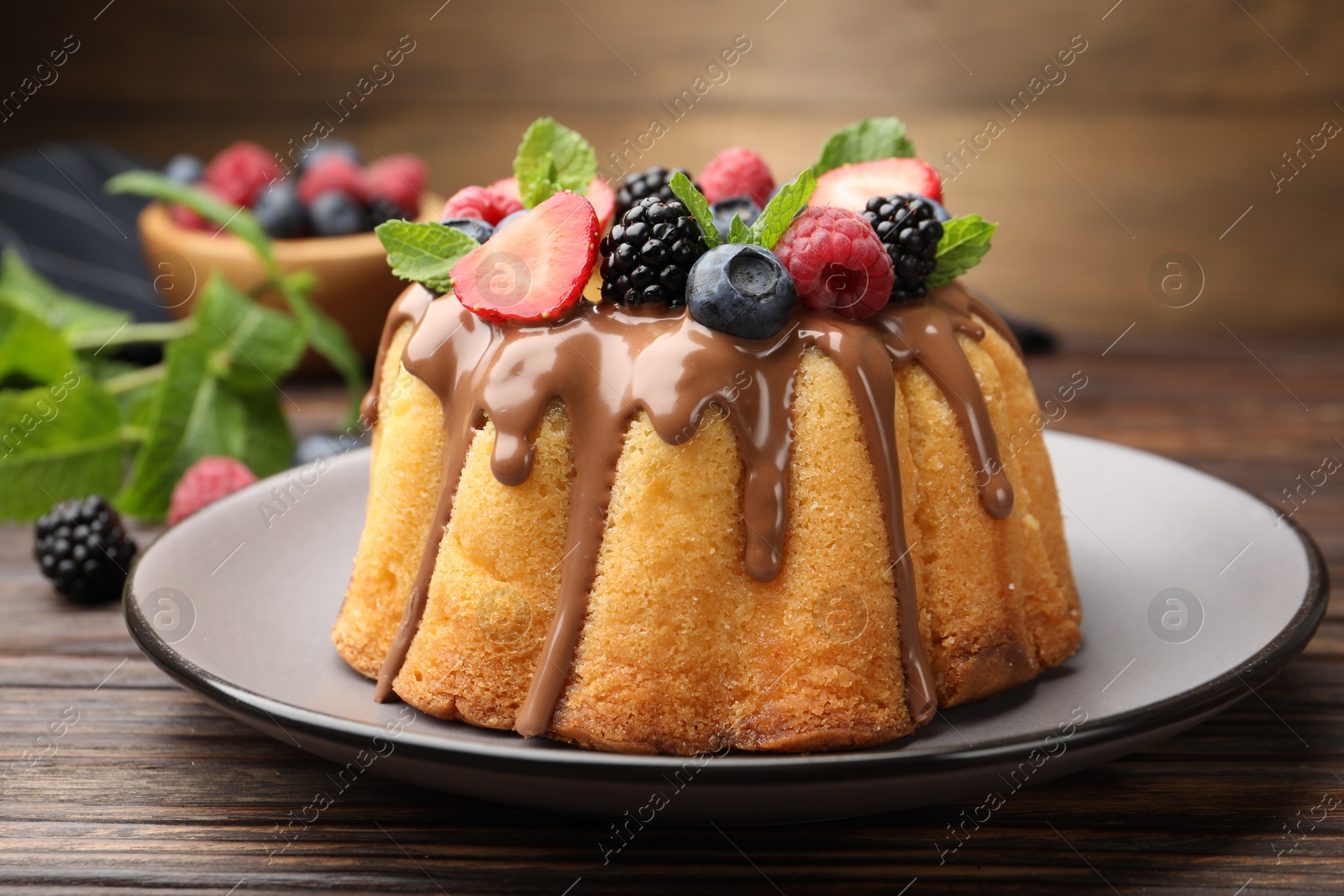 Photo of Tasty Bundt cake with berries, chocolate and mint on wooden table, closeup