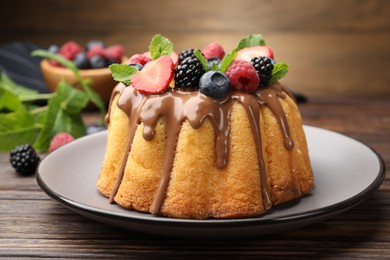 Photo of Tasty Bundt cake with berries, chocolate and mint on wooden table, closeup