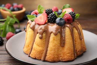 Photo of Tasty Bundt cake with berries, chocolate and mint on wooden table, closeup
