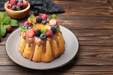 Photo of Tasty Bundt cake with berries, chocolate and mint on wooden table, closeup. Space for text