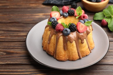 Photo of Tasty Bundt cake with berries, chocolate and mint on wooden table, closeup