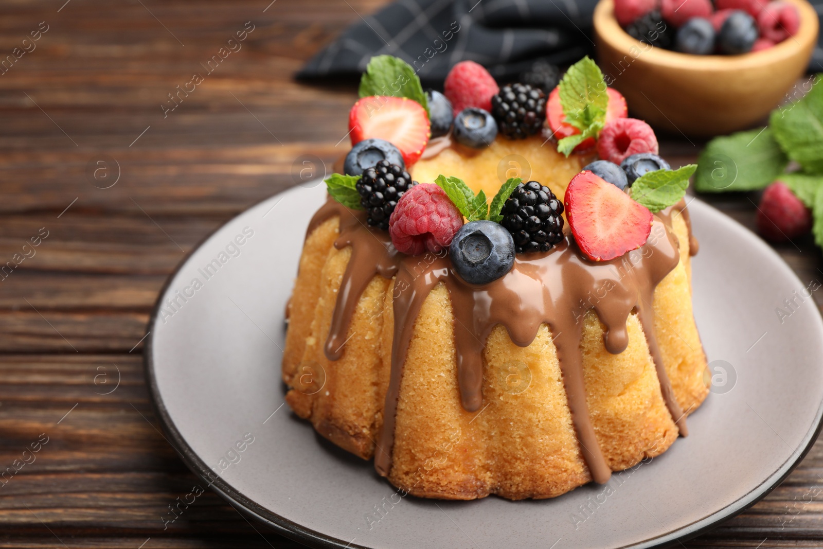 Tasty Bundt cake with berries, chocolate and mint on wooden table, closeup Photo of Tasty Bundt cake with berries, chocolate and mint on wooden table, closeup